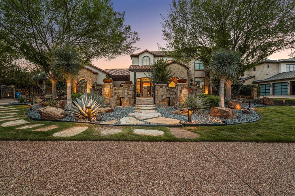 Front elevation at dusk, stone-and-stucco facade with iron entry gate and desert-modern xeriscape