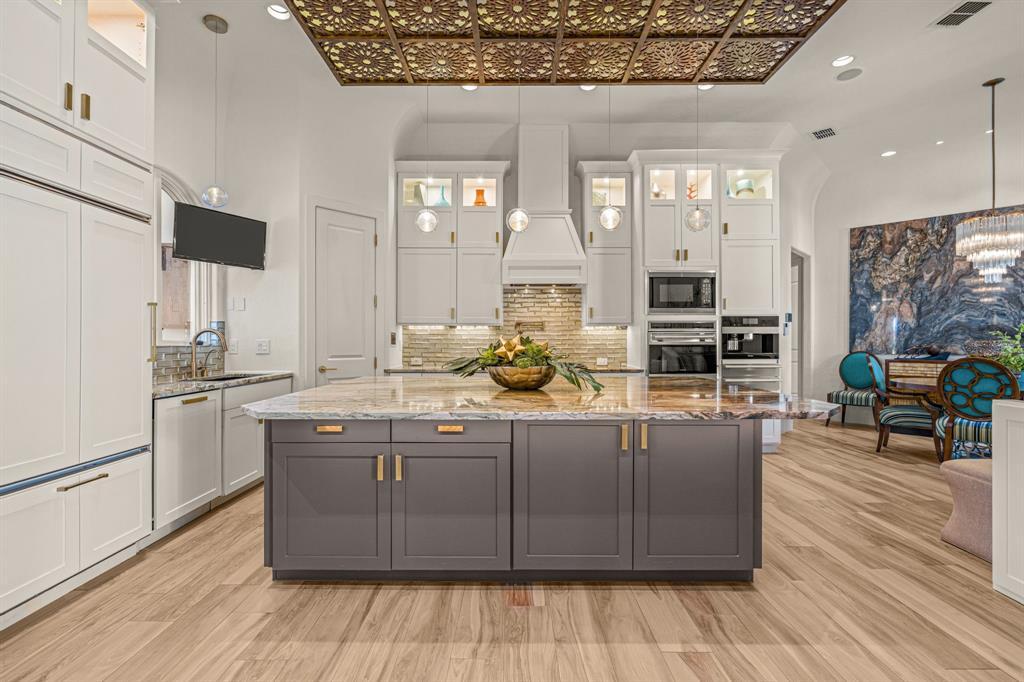 Chef's kitchen with a granite-waterfall island, white cabinetry and a gilded coffered ceiling panel