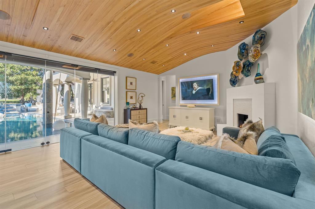 Family room with a teal sectional, lit white fireplace and sculptural wood-beamed ceiling