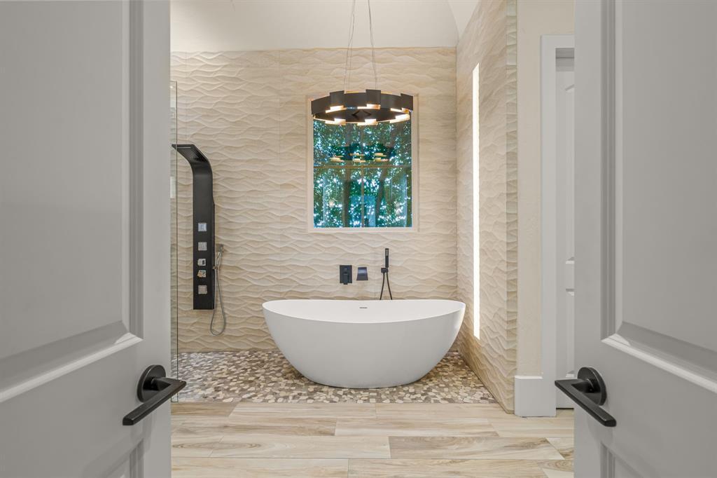 The primary bath with a freestanding soaking tub beneath a ring chandelier and wave-textured tile