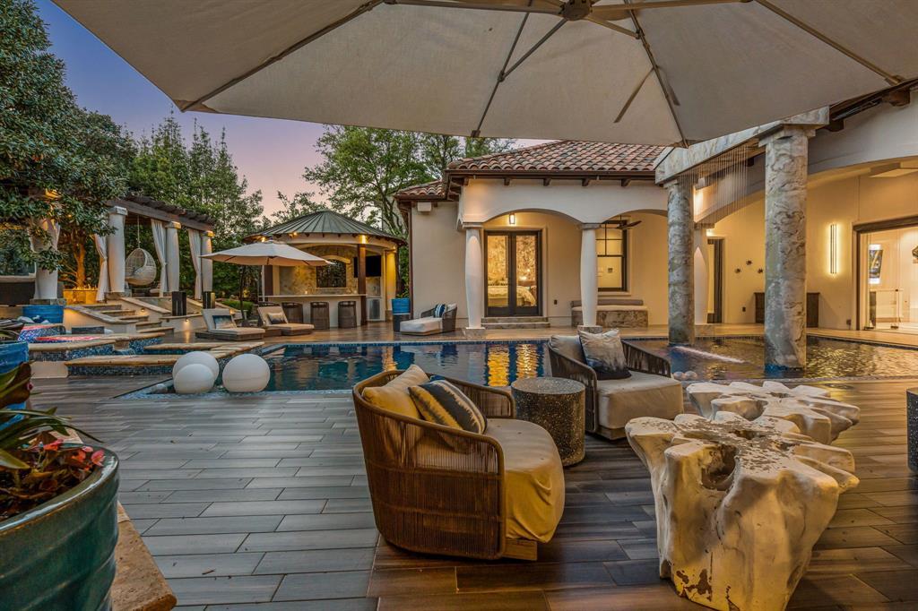 Wide view of the backyard with pool, spa and a covered outdoor-kitchen pavilion at dusk