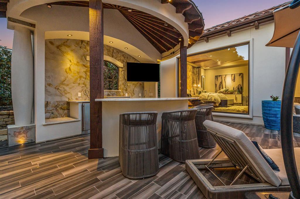 Outdoor kitchen and bar with an onyx-lit backsplash and rattan stools under a sunburst wood ceiling