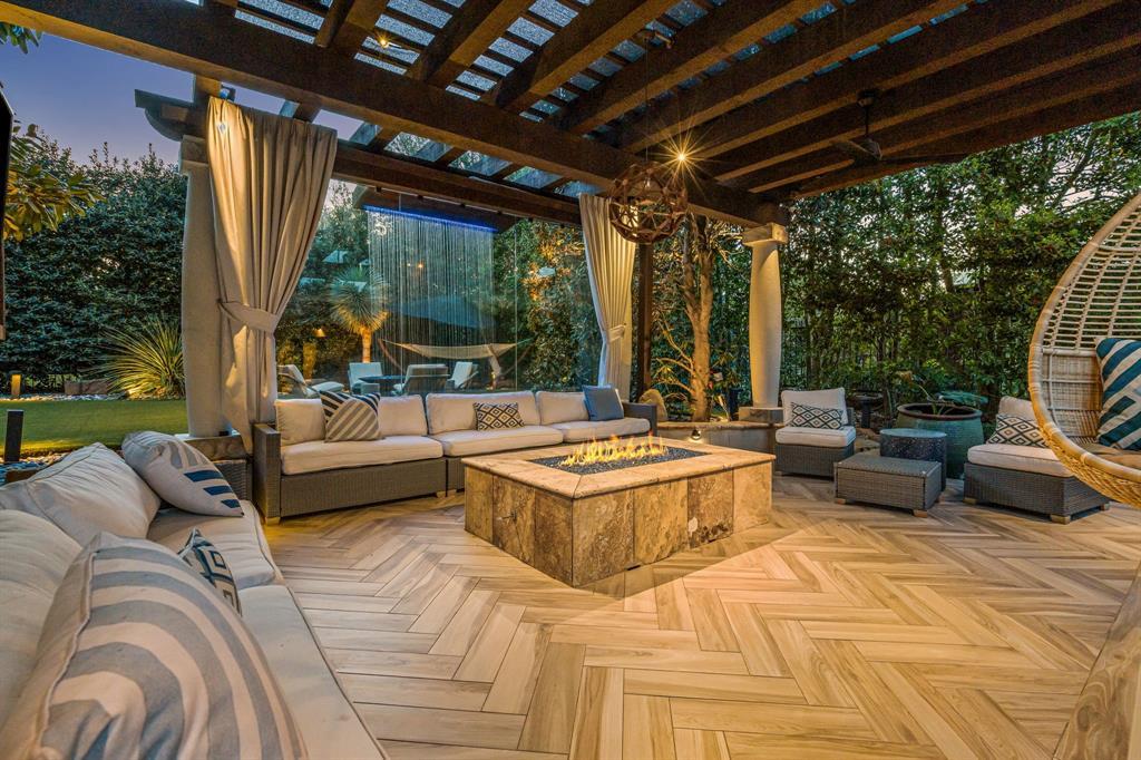 The backyard fire-pit lounge at dusk, a lit stone gas fire pit, wicker sectionals, putting green beyond