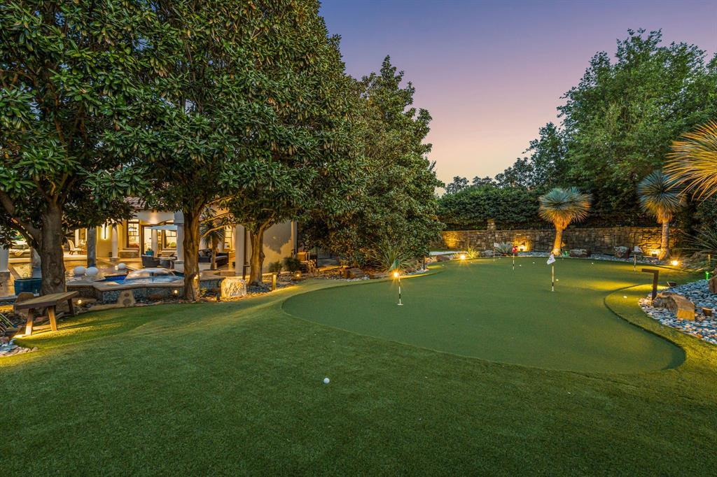 The multi-hole putting green uplit at dusk with a stone boundary wall and the house glowing beyond